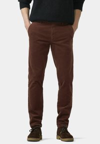 Pantalon en velours côtelé marron à coupe slim, avec poches avant et texture lisse, associé à des chaussures en daim foncé.