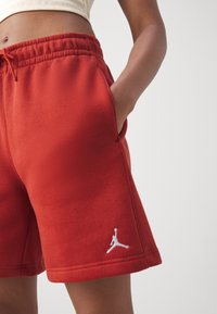 Shorts en polaire rouge avec une taille élastique et un cordon de serrage ; dotés de poches latérales et d'un logo Jumpman brodé en blanc sur l'ourlet.