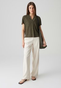 Top verde oliva a maniche corte con scollatura a V; abbinato a pantaloni larghi beige e infradito nere; con una borsa tote grigia texturizzata.