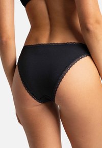 Sous-vêtements noirs en coton avec une bordure en dentelle le long de la ceinture et des ouvertures des jambes. Le design présente une forme classique de slip et une texture lisse.