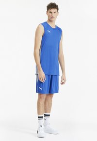 Canottiera atletica blu e pantaloni corti realizzati in tessuto leggero, con logo Puma. Abbinati a sneakers bianche e calze a righe.