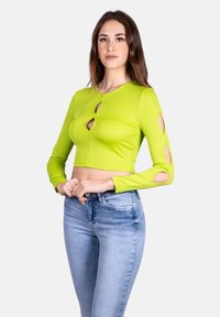 Top lungo a maniche corte verde lime con dettagli a taglio sulle maniche e scollo rotondo, abbinato a jeans skinny azzurri.