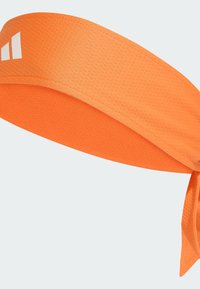 Cinta para la cabeza de tela naranja con un patrón texturizado, que presenta un diseño anudado en la parte posterior y un pequeño logo blanco en la parte delantera.