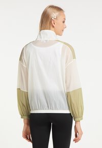 Giacca leggera realizzata in tessuto trasparente con pannelli beige e verde oliva, polsini elasticizzati e design con colletto alto, adatta per essere indossata a strati.