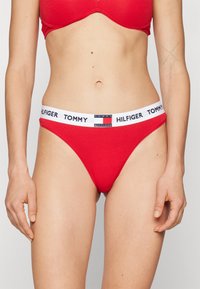 Bikini en coton rouge avec une taille élastique blanche portant le logo "TOMMY HILFIGER". Le design est minimaliste avec une texture lisse.