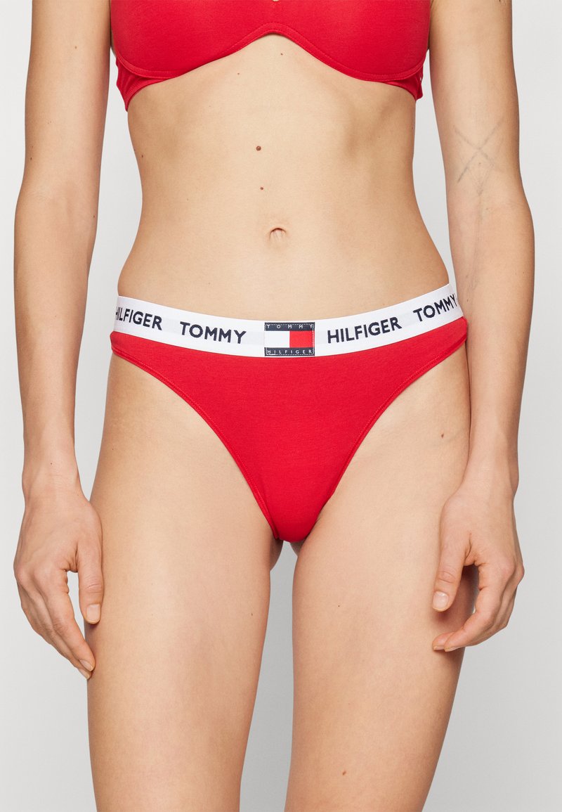 Bikini en coton rouge avec une taille élastique blanche portant le logo "TOMMY HILFIGER". Le design est minimaliste avec une texture lisse.