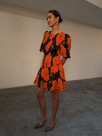 Abito floreale in arancione e nero con maniche a sbuffo, corpetto aderente e gonna svasata. Indossato con tacchi in stampa leopardata.