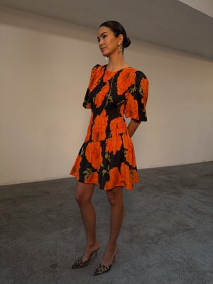 Abito floreale in arancione e nero con maniche a sbuffo, corpetto aderente e gonna svasata. Indossato con tacchi in stampa leopardata.