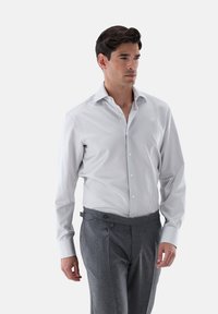 Weißes Hemd mit schmalen grauen Streifen, Button-Down-Kragen, lange Ärmel. Kombiniert mit grauen gefalteten Hosen. Glatte Textur.