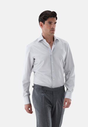 Weißes Hemd mit schmalen grauen Streifen, Button-Down-Kragen, lange Ärmel. Kombiniert mit grauen gefalteten Hosen. Glatte Textur.