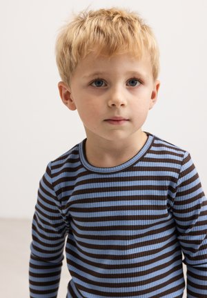 Blond lille dreng med blå øjne iført en blå og brun stribet langærmet skjorte, der kigger lidt væk fra kameraet mod en ensfarvet baggrund.