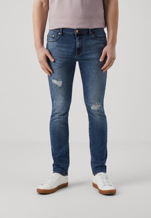 Bla jeans med slim fit, med slitte lapper og frayed kanter, paret med hvite joggesko. Glatt tekstur og klassisk design.