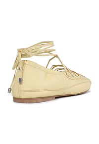 Chaussure plate en cuir jaune avec un bout rond, un design ouvert et des lanières croisées. Elle dispose d'une semelle plate et d'une texture lisse.