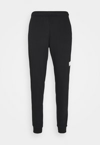 Pantalons de survêtement noirs avec une coupe ajustée, fabriqués à partir d'un tissu doux. Ils sont dotés d'une taille élastique et d'un accent logo blanc sur le côté.