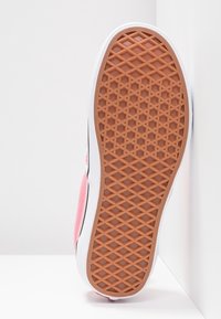 Chaussure vue du côté de la semelle, montrant le motif nervuré en caoutchouc brun, la partie supérieure en tissu rose et la semelle intermédiaire blanche avec une bande noire.