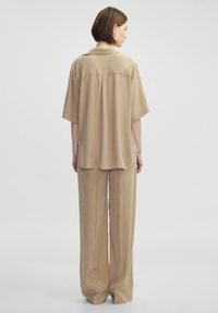 Beige two-piece outfit featuring a short-sleeve, collared shirt and wide-leg trousers, made of lightweight fabric with a smooth texture.