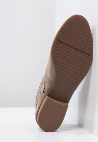 Béžová bota s perforovaným vzorem, s texturovanou podešví s embosovaným nápisem "Tamaris". Velikost 37 je uvedena na patě.
