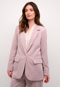 Blazer de microcordón rosa claro con solapas de muesca, dos bolsillos frontales y un corte relajado. Textura acanalada vertical en toda la tela.