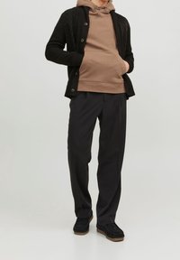 Cárdigan negro de punto sobre una sudadera marrón, combinado con pantalones negros y zapatos oscuros. Presenta botones y un diseño de tela texturizada.