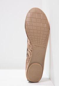 Suela de zapato color canela con un patrón de agarre texturizado. Presenta un acabado superior en bronce metálico y el logo de la marca "Tamaris". Tamaño 39 indicado.