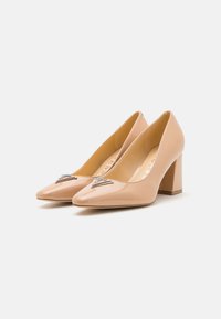 Pumps beige in pelle verniciata con tacco alto e punta affilata, arricchiti da dettagli decorativi in argento sulla parte anteriore. Design con tacco a blocco per maggiore stabilità.