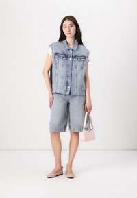 Gilet senza maniche in denim azzurro chiaro con due taschini frontali, abbinato a pantaloni corti in denim lunghi fino al ginocchio. Presenta una borsa rosa e scarpe basse beige.