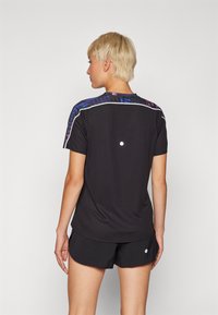 Camiseta atlética preta com padrão colorido nos ombros, mangas curtas e barra curva. Apresenta um pequeno detalhe de ponto nas costas.