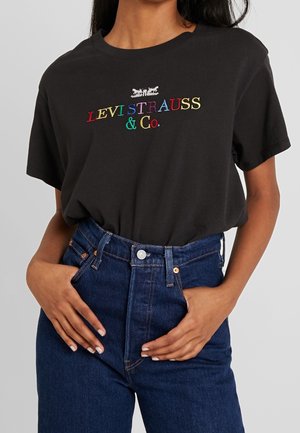 T-shirt noir en coton avec le logo "LEVI STRAUSS & Co." multicolore cousu. Porté avec un jean en denim bleu taille haute.