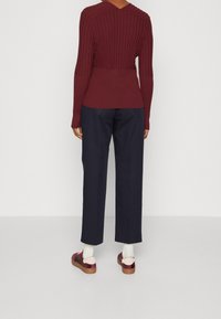 Viininpunainen ribbineulottu neule V-aukkokoristeella ja teksturoidulla selällä, yhdistetty tummansinisiin housuihin ja kiiltäviin viininpunaisiin lenkkareihin, joissa on vaaleanpunaiset koristeet.