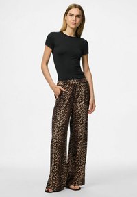 T-shirt noir à manches courtes associé à un pantalon large en imprimé léopard affichant des taches marron et noires ; le tissu semble doux et léger.