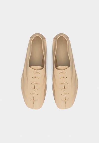 Ζευγάρι μπεζ μαλακά δερμάτινα μινιμαλιστικά παπούτσια με κοντό κορδόνι, σε θέα από πάνω πάνω σε λευκό φόντο.