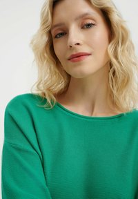 Grüner Strickpullover mit weitem Ausschnitt und strukturiertem Stoff. Weiches, leichtes Material mit lockerer Passform und sichtbaren Rippen Details.