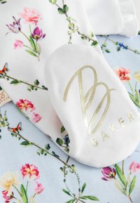 Primo piano di un tessuto con motivo floreale con una patch bianca che presenta l'elegante scritta logo "B BAKER" in oro.