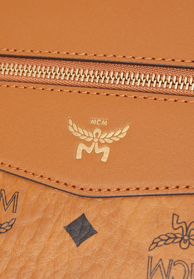 Portefeuille en cuir tan avec un logo doré, fermeture éclair et couture décorative. Comprend des motifs en diamant noirs sur une surface texturée.