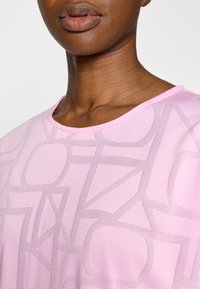 Ροζ μπλουζάκι με κοντά μανίκια που διαθέτει διακριτικό γεωμετρικό σχέδιο και απαλή υφή. Στρογγυλή λαιμόκοψη με απλές άκρες.