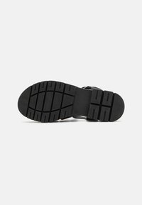 Suela de zapato de goma negra con un patrón de relieve texturizado, que presenta profundas ranuras para mayor agarre y una forma de puntera redondeada.