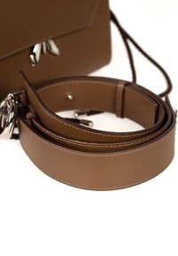 Brun læderhank med glat tekstur, flad form og hvid syning. Har metalhardware og en løkke til fastgørelse.