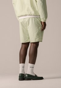 Ensemble de veste et de shorts vert clair en tissu texturé, associé à des mocassins verts et des chaussettes blanches avec des inscriptions noires, vu de dos.