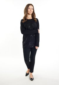 Schwarzer langärmliger Paillettenpullover mit lässiger Passform, kombiniert mit taillierten schwarzen Hosen und spitzen schwarzen High Heels.