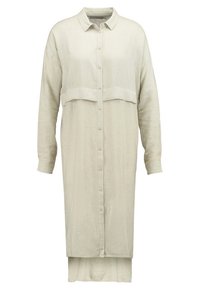 Robe chemise en lin beige clair avec manches longues, fermeture à boutons discrets sur le devant et un design en couches avec une couture au niveau du milieu.