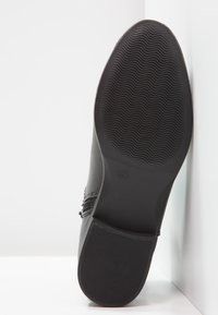 Schwarze Schuhsohle mit einem glatten, strukturierten Muster. Das Material wirkt gummiert und weist ein dezentes Logo sowie abgerundete Kanten für ein elegantes Design auf.