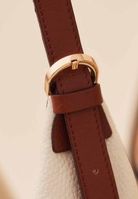 Brown leather strap with a gold-toned metal buckle, detailed stitching, and soft textured white leather background.