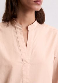 Blusa di cotone color pesca con colletto alla mandarino, maniche corte e patta centrale. Texture liscia e leggero lucido.