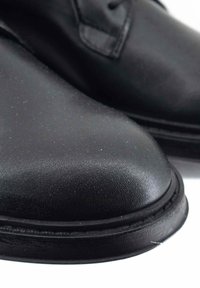 Scarpe in pelle nera con punta arrotondata, texture liscia e cuciture a contrasto lungo la suola. Dettagli hardware minimi.