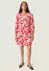 Vestido floral rojo con escote en V y mangas largas abullonadas. Presenta un corte holgado y una textura suave. Se lleva con zapatos planos negros.