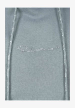Hellblaues Sweatshirt mit taillierter Passform, mit durchgehendem Reißverschluss und geprägtem Logo-Detail. Glatte Textur mit subtilen Nähten.