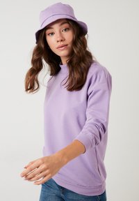 Felpa lilla con maniche lunghe e colletto a girocollo, abbinata a un cappello a secchiello lilla coordinato. Il tessuto sembra morbido e texturizzato.