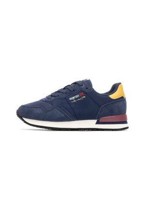 Zapatilla deportiva de color azul marino con parte superior de ante y malla, diseño con cordones, acento amarillo en el talón, entresuela blanca y suela exterior de goma negra.