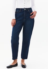 Vaqueros de tiro alto azul oscuro con un diseño de pierna recta, cinco bolsillos, costuras cosidas y un cierre de botón en la cintura.