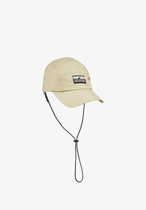 Beige kasket lavet af letvægtsmateriale, med en buet skygge, justerbar hagerem og et patch med teksten "Lavet til daglige eventyr".